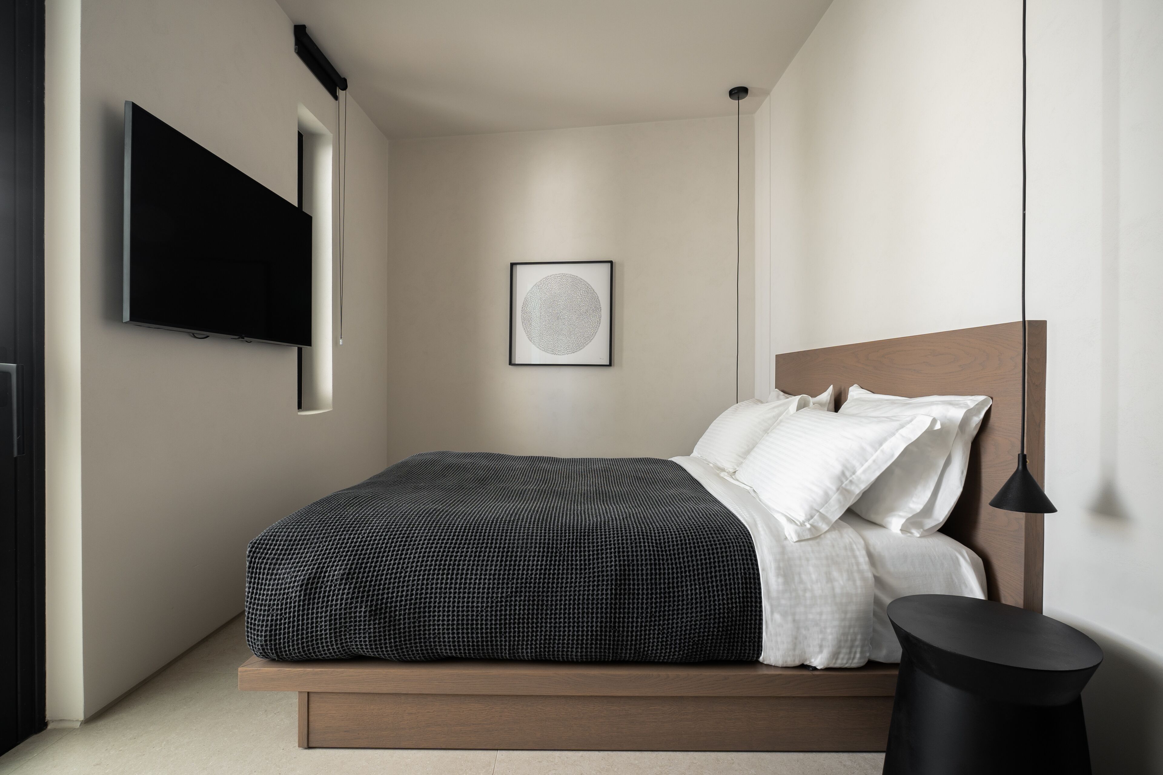 A modern bedroom with a bed, a mounted TV, a framed artwork, and a bedside table.