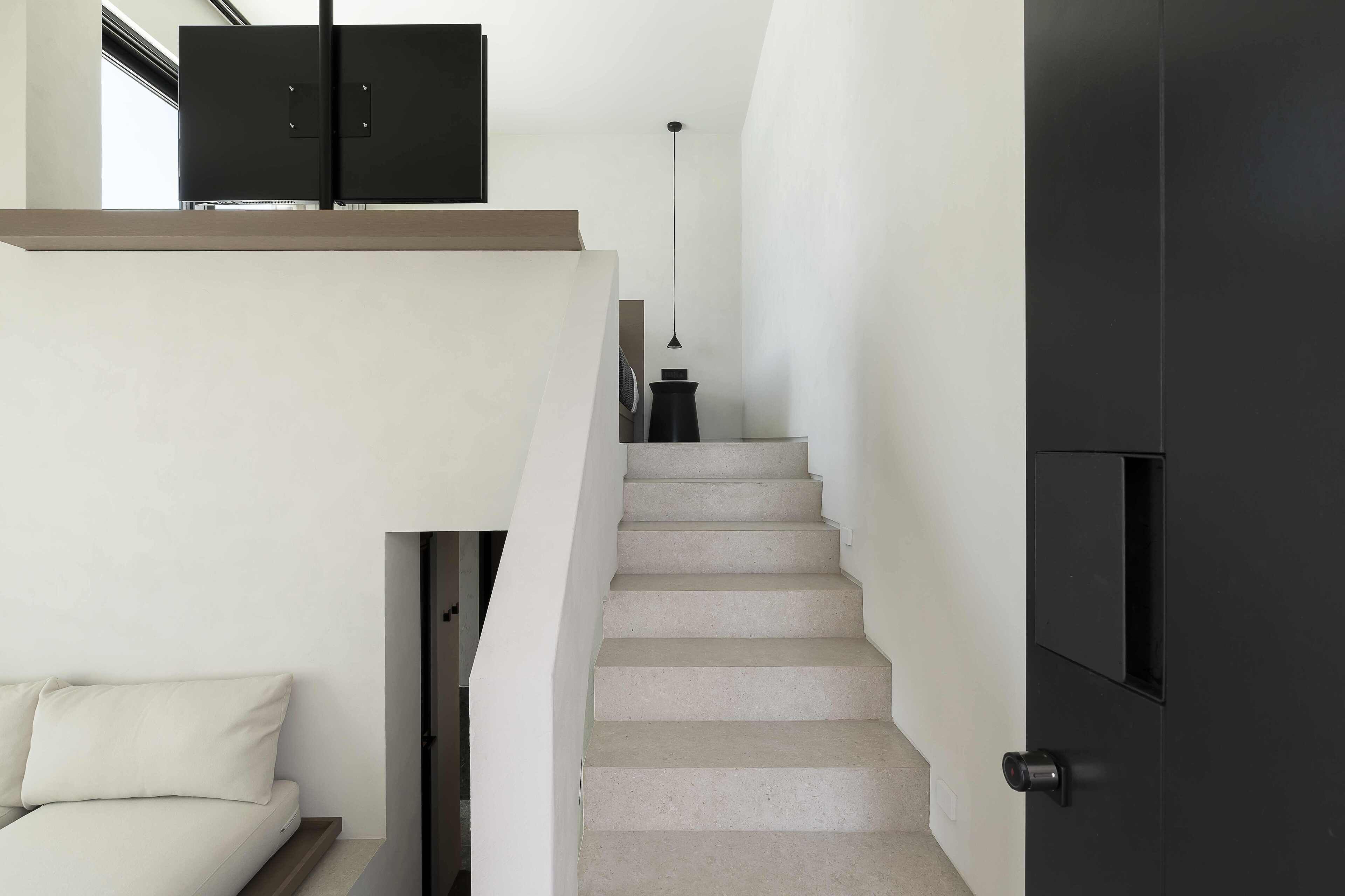 Eine moderne Treppe mit minimalistischem Design, eine Couch mit Kissen und eine Pendelleuchte.