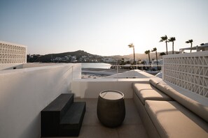 Eine Dachterrasse mit Meerblick, eine Sitzecke mit Kissen, ein großer runder Tisch und ein weißes Geländer.