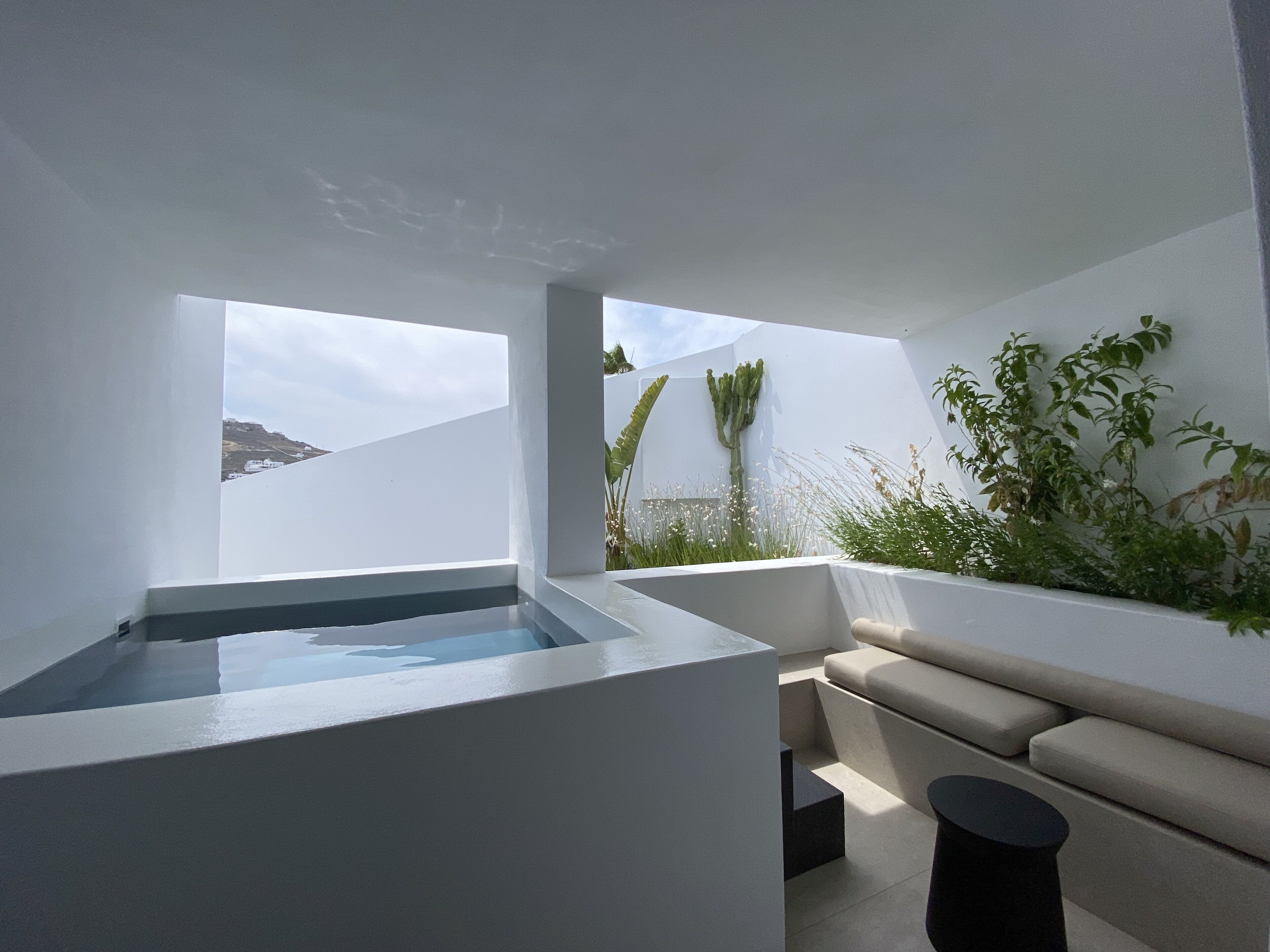 A modern outdoor terrace with a minimalist design, featuring a seating area, a water feature, and a view of the landscape.