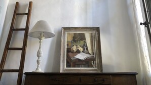 Huoneessa on puinen katto, valkoinen seinä, puinen kaappi, kehystetty maalaus ja lamppu.