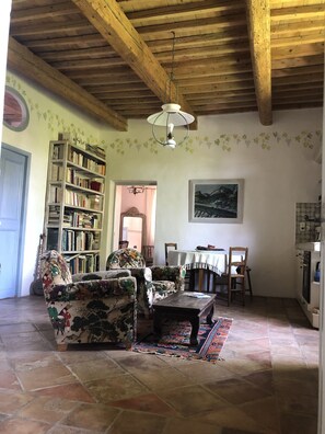 A cozy living room with a wooden ceiling, a bookshelf, a patterned sofa, and a dining area.
