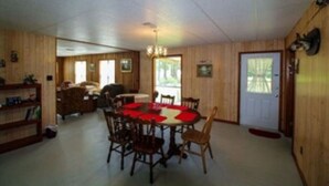 A dining area with a round table, chairs, and a chandelier. There is a door with a mat in front of it.