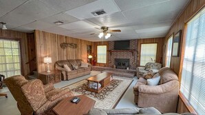 A cozy living room with a fireplace, wooden walls, and a ceiling fan.