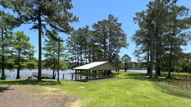 A lakeside park with a covered pavilion, a grassy area, and tall trees.
