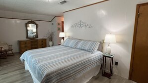 A bedroom with a bed, bedside lamps, a dresser, a mirror, and a decorative wall piece.