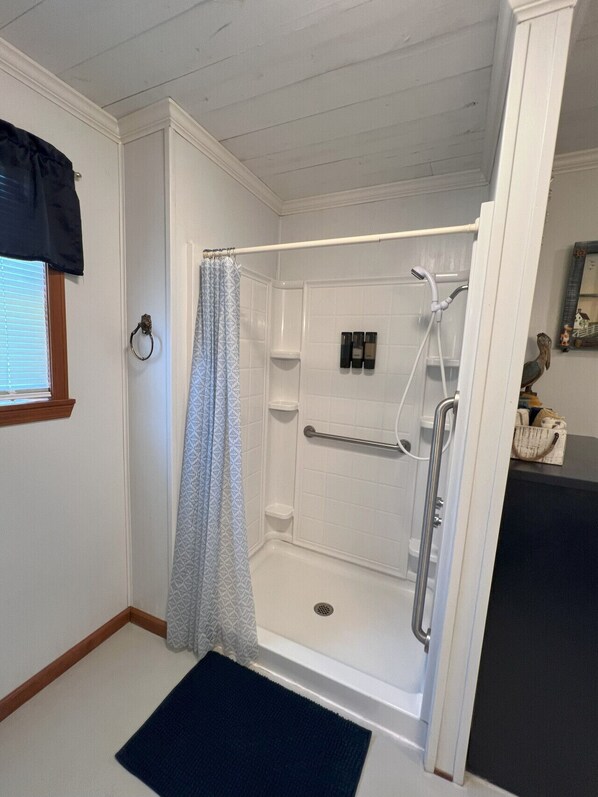 A walk-in shower with a showerhead, a towel rack, and a small shelf with toiletries.