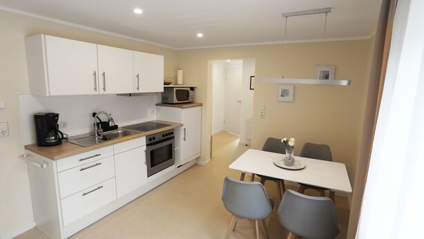 A compact kitchen with white cabinets, a microwave, a coffee maker, and a dining area with a table and chairs. - Moderne Ferienwohnung in Kassel (Kassel)