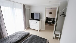 A bedroom with a bed, a TV on a dresser, a small white table, and a view into another room. - Moderne Ferienwohnung in Kassel (Kassel)