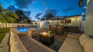 A backyard with a pool, outdoor seating, and a fire pit.