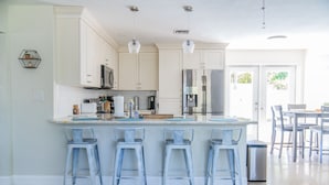 A modern kitchen with white cabinets, a central island with bar stools, stainless steel appliances, and a view to the outside.