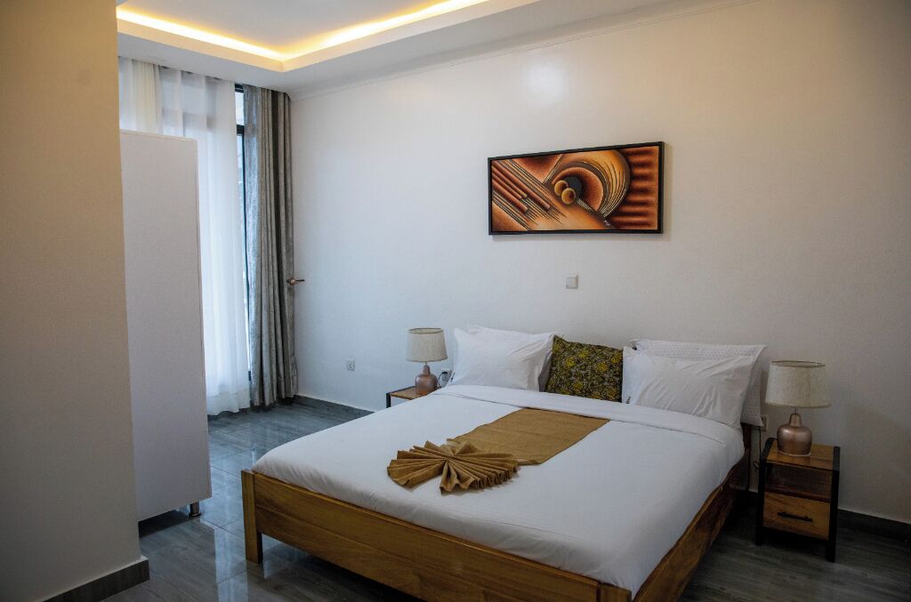 Een hotelkamer met een groot bed, twee nachtkastjes, een wanddecoratie en uitzicht buiten door een raam met gordijnen.