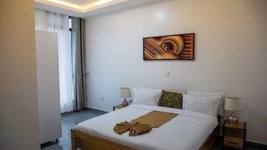 A hotel room with a large bed, two bedside tables, a wall-mounted artwork, and a view of the outside through a window with curtains.