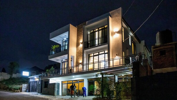 A modern two-story building with a balcony, large windows, and outdoor seating area.