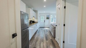 Una cocina moderna con armarios blancos, un refrigerador de acero inoxidable y piso de madera.