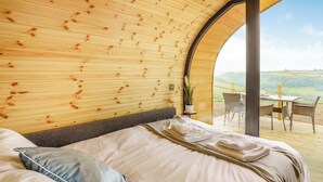 Ein gemütliches Zimmer mit Holzbalkendecke, einem Bett mit ordentlich gefalteten Handtüchern und Blick auf eine grüne Landschaft durch ein großes Fenster.