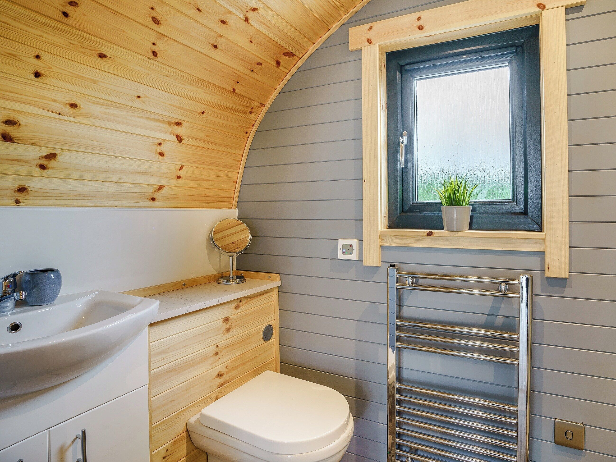 Et lille badeværelse med træloft, et vindue med udsigt, vask og toilet.