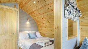 Ein gemütliches Schlafzimmer mit Holzboden, einem Bett mit weißen Leinentüchern, einem blauen Kopfkissen und einem Fenster mit Vorhängen.