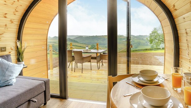 Ein gemütliches Zimmer mit Holzvertäfelung, einer Couch, einem Esstisch mit Tellern und Gläsern sowie Blick auf die Landschaft.