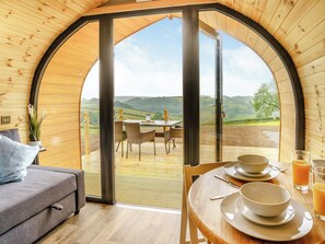 Una habitación acogedora con detalles de madera, un sofá, una mesa de comedor con platos y vasos, y vistas al campo.