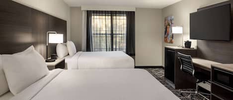A hotel room with two beds, a desk, a chair, a TV, and a window with curtains.