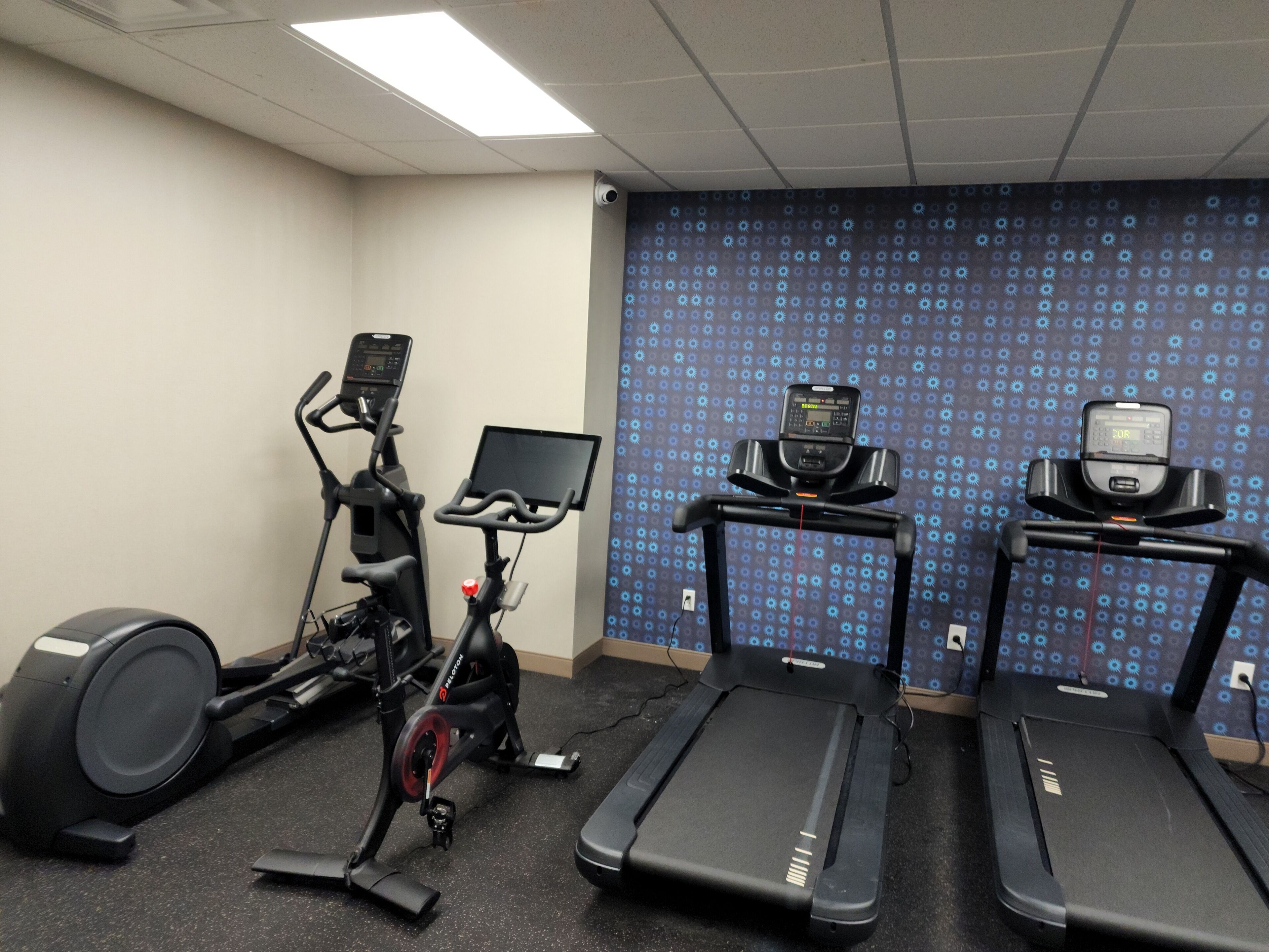 Un gimnasio con bicicletas estáticas, cintas de correr y una pantalla en la pared.
