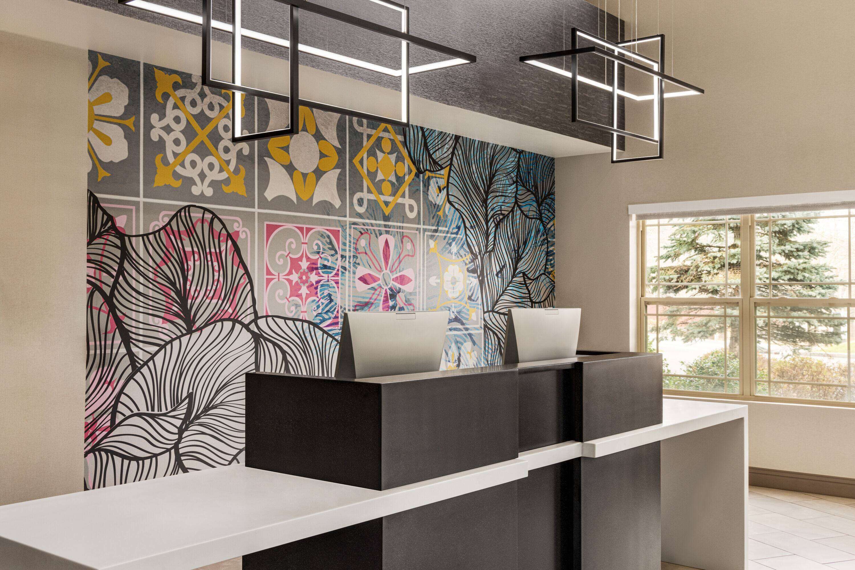 A reception desk with a modern design, a patterned wall, and a window providing a view of trees.