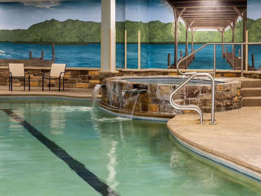 An indoor swimming pool with a waterfall feature, stone steps, and a view of a painted landscape.