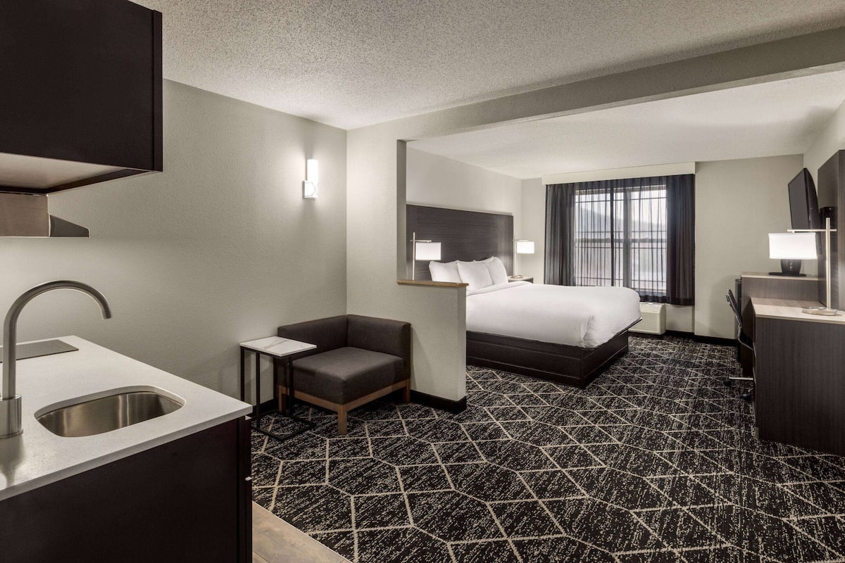 Ein Hotelzimmer mit Bett, Schreibtisch, Stuhl, Waschbecken und einem Fenster mit Vorhängen.