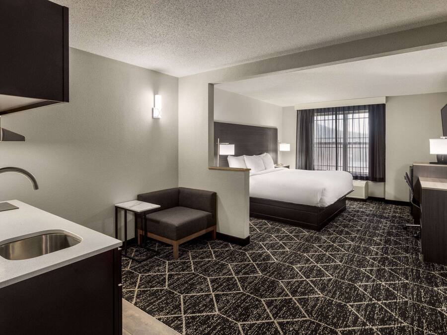 Habitación de hotel con cama, escritorio, silla, lavamanos y ventana con cortinas.