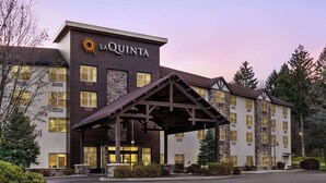 Un hotel con un llamativo letrero de 'LAQUINTA', un acceso cubierto y un estacionamiento.