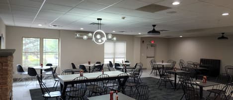 Un vaste espace de restauration intérieur, doté de nombreuses tables et chaises, de grandes fenêtres et de luminaires au plafond.