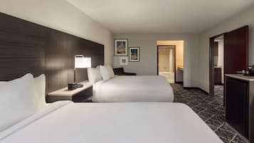 A hotel room with two beds, a desk with a lamp, a wardrobe, and framed pictures on the wall.