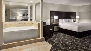 Habitación de hotel con una bañera grande, una cama con ropa de cama blanca, un cabecero oscuro y un suelo con estampado blanco y negro.