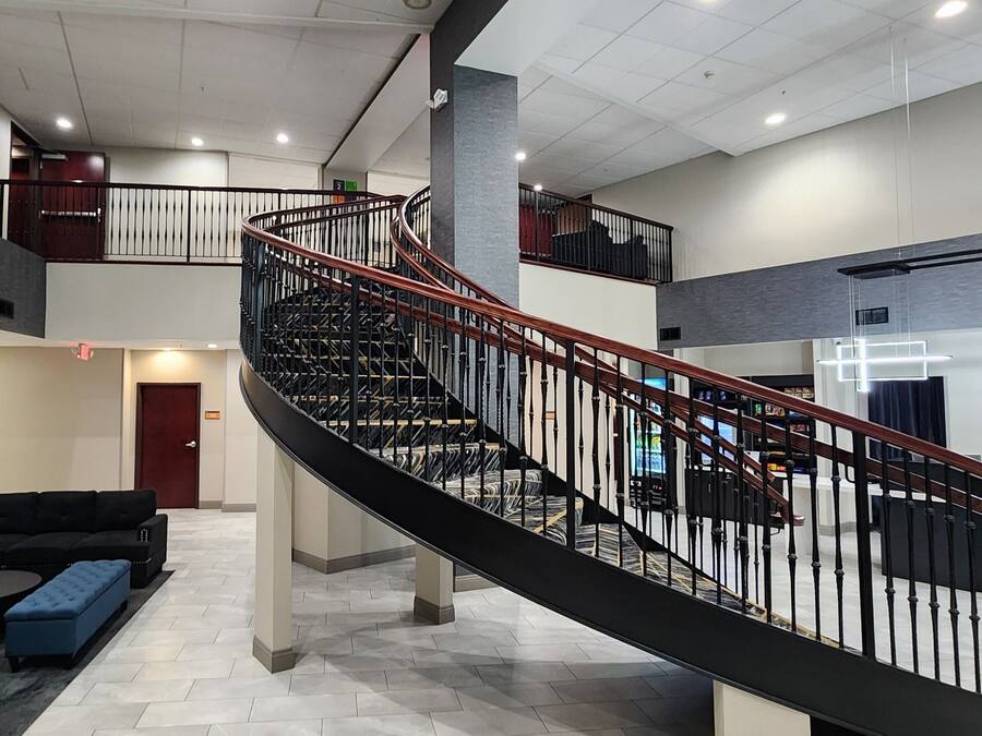 A spacious lobby with a curved staircase, a black leather sofa, a blue ottoman, and a coffee table with a vase of red flowers.