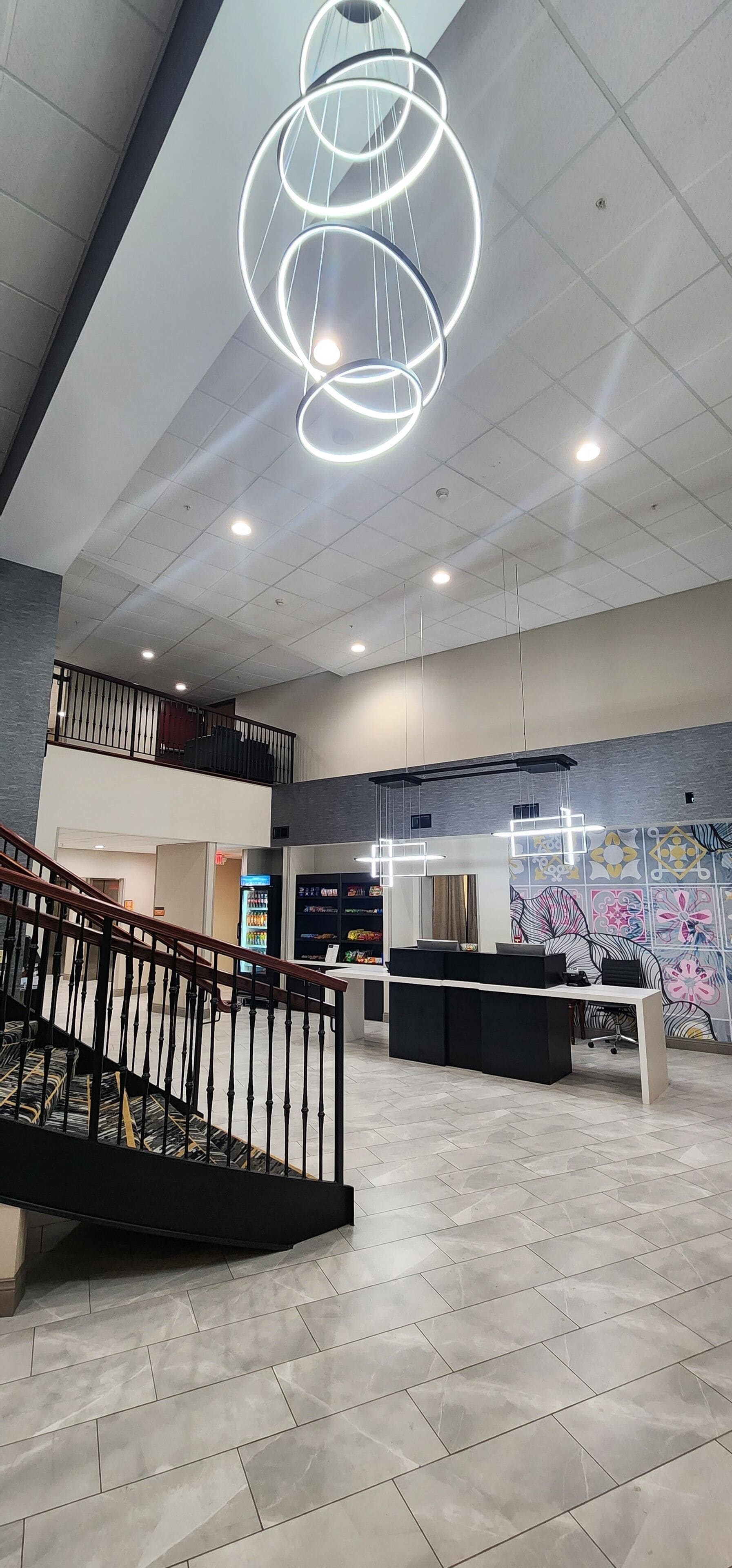 A spacious lobby with a modern staircase, a reception desk, and a decorative wall mural.