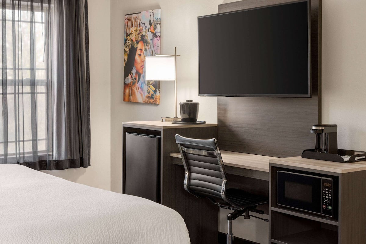 Ein Hotelzimmer mit Bett, Schreibtisch, Stuhl, Fernseher und Mikrowelle.