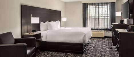 A hotel room with a large bed, a desk, a chair, a TV, and a window with curtains.