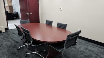 A conference room with a round table, six chairs, a red cabinet, and a fire alarm on the wall.
