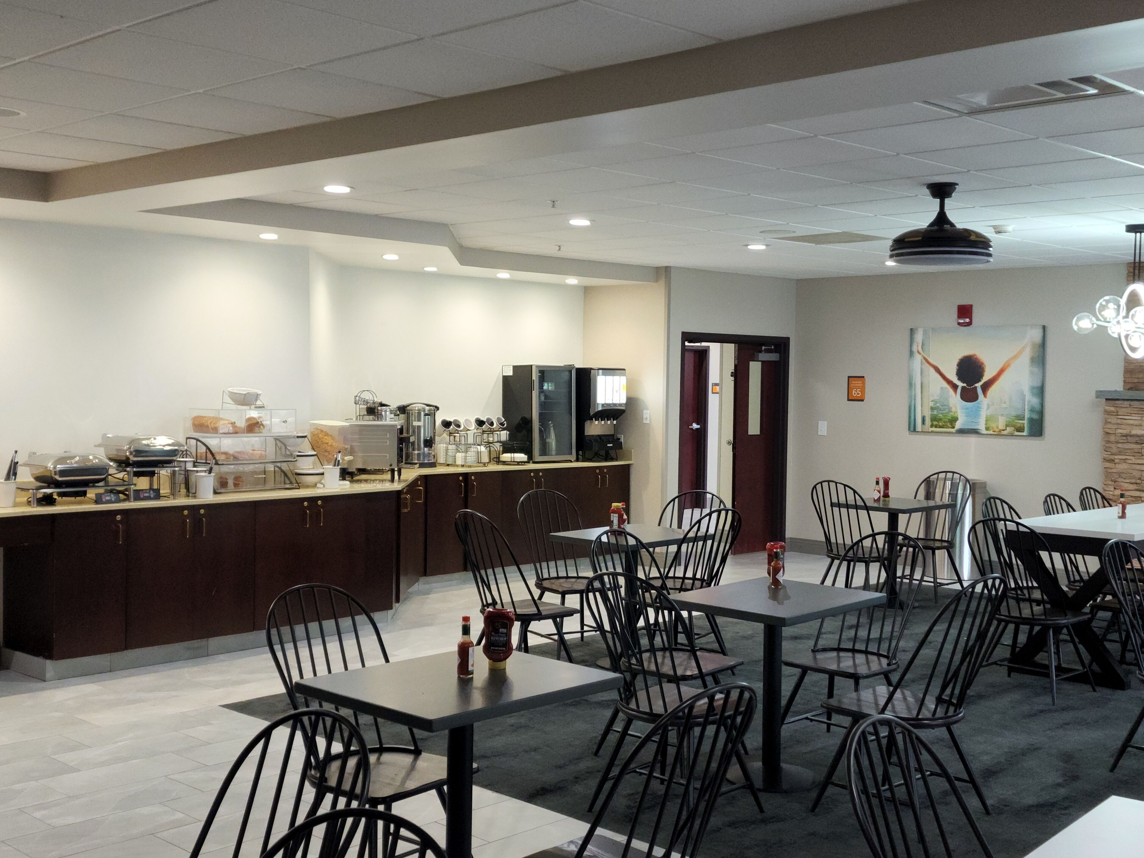 A dining area with tables and chairs, a kitchen area with appliances, and a painting on the wall.