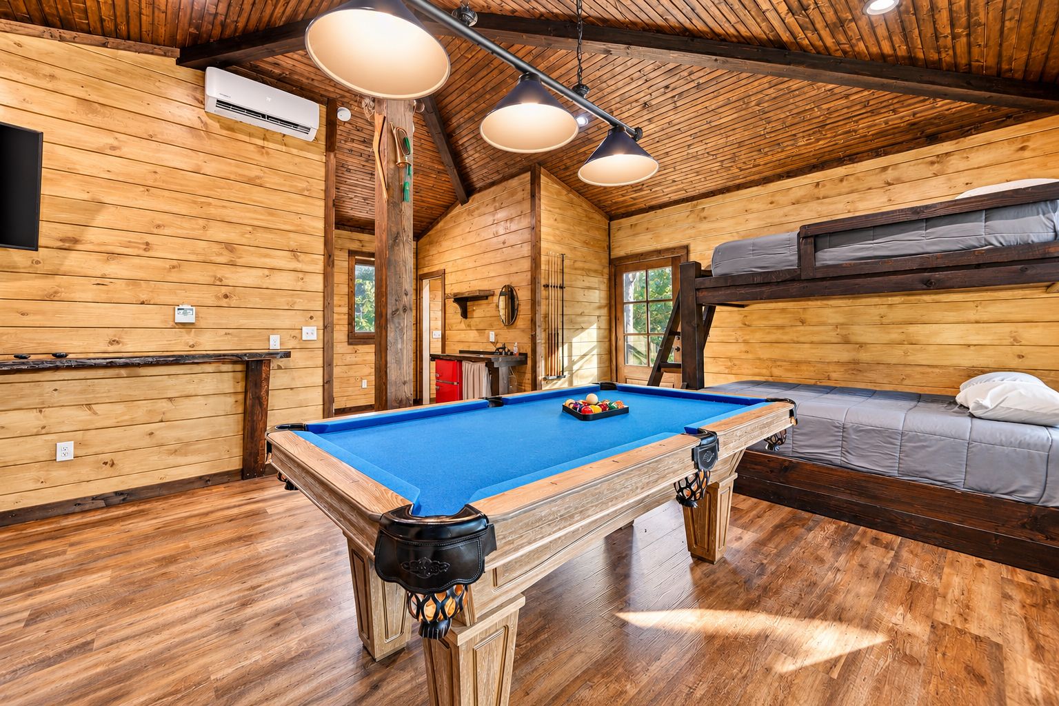 Une pièce en bois avec une table de billard, des lits superposés et un ventilateur de plafond.