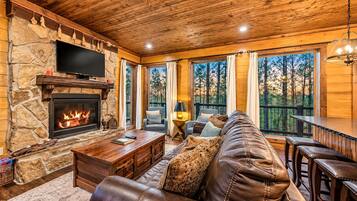 A cozy living room with a stone fireplace, leather sofa, and a large TV.