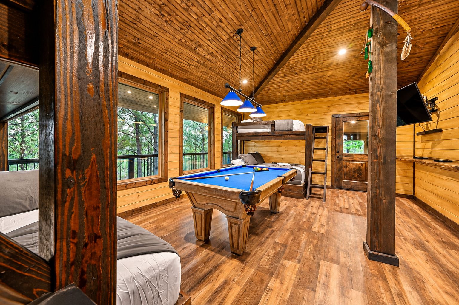 A wooden interior with a pool table, bunk beds, and a television.