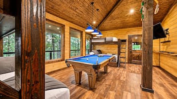 A wooden interior with a pool table, bunk beds, and a television.