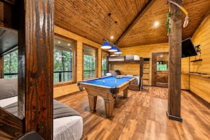 A wooden interior with a pool table, bunk beds, and a television. - 3 Story Treehouse | Views, Pool Table, Hot Tub (Broken Bow)