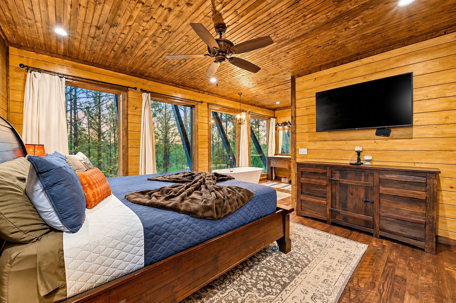 Ein Schlafzimmer mit Bett, Fernseher, Bad und großen Fenstern.