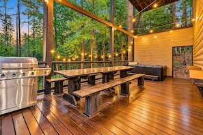 An outdoor wooden deck with a grill, picnic table, and string lights. - 3 Story Treehouse | Views, Pool Table, Hot Tub (Broken Bow)