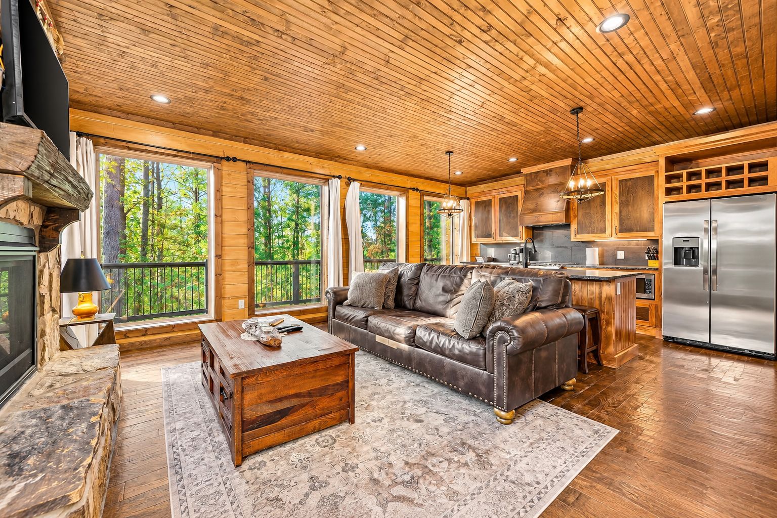 A spacious living room with a leather sofa, wooden coffee table, and large windows offering a view of the outdoors.