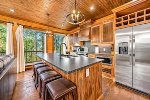 A modern kitchen with a large island, stainless steel appliances, and wooden cabinetry. - 3 Story Treehouse | Views, Pool Table, Hot Tub (Broken Bow)
