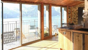 Un balcó espaiós amb vista a un llac i muntanyes, sòl de fusta i zona de cuina amb una pica i armaris.